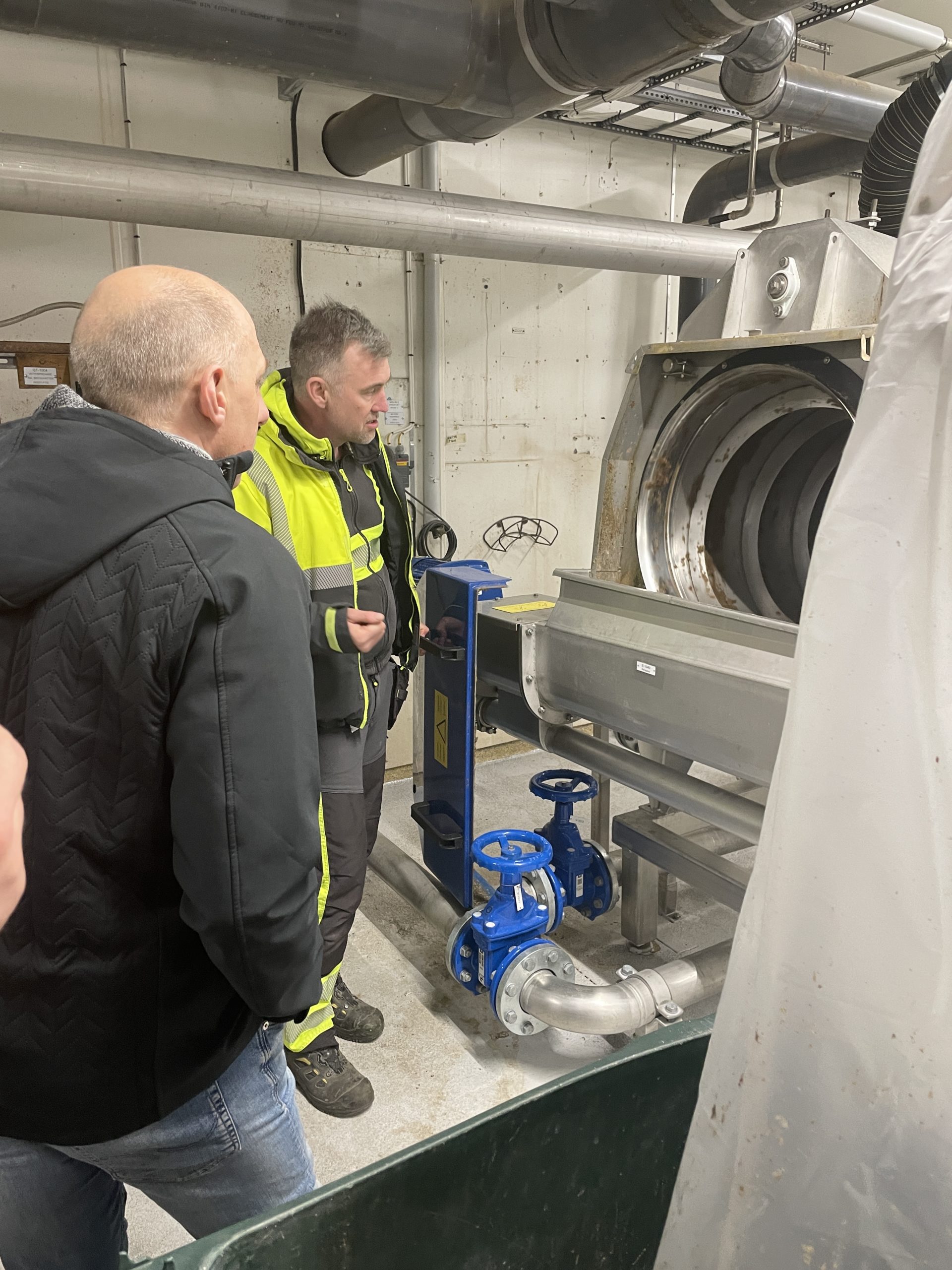 Två personer som tittar på en maskin på reningsverket.
