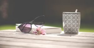 solglasögon, en öppen bok och en mugg med te eller kaffe