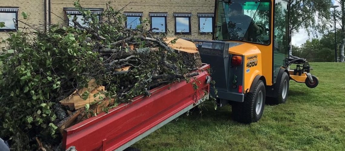 Trädgårdstraktor med släpvagn lastad med trädgrenar