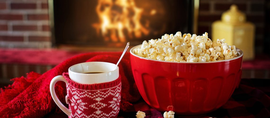 En mugg, en skål popcorn och en mysig brasa i bakgrunden.
